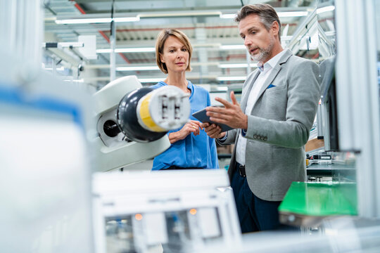 Businessman with tablet and woman talking at assembly robot in a factory