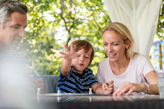 Happy parents and son playing a board game on terrace