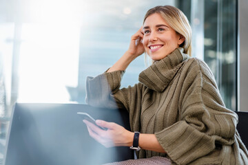 Young woman in a sweater holding a cell phone and smiling indoors
