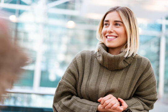 Young woman in a sweater smiling indoors in a modern urban setting