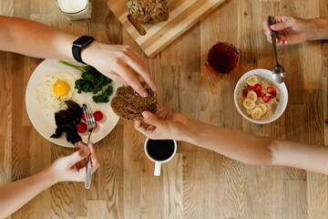 Hands passing bread over a breakfast table with various foods