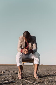 Pensive young man sitting on chair in barren land