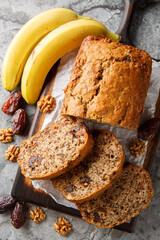 Vegetarian date banana walnuts bread loaf with honey and spices close-up on wooden board on table. Vertical top view from above