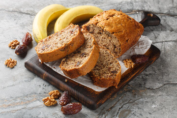 Freshly baked date banana walnuts bread loaf surrounded by ingredients close-up on wooden board on table. Horizontal