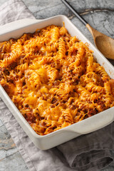Sloppy Joe Casserole is loaded with juicy ground beef and pasta smothered in a cheesy sauce closeup in the baking dish on the table. Vertical
