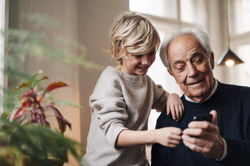 Happy grandfather and grandson using cell phone at home