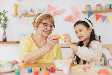 Happy grandmother and granddaughter in easter bunny ears having egg tapping with easter eggs