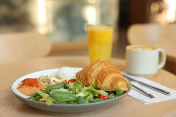 Tasty breakfast. Freshly baked croissant and salad served on wooden table in cafe, closeup