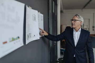 Senior businessman looking at papers hanging on the wall