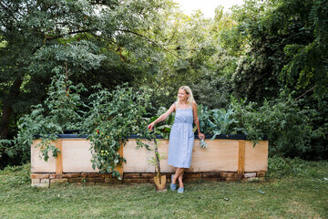 Blond smiling woman standing in front of her raised bed in her own garden