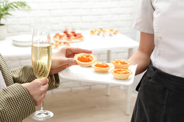 Woman taking tasty canape from waiter with board indoors, closeup