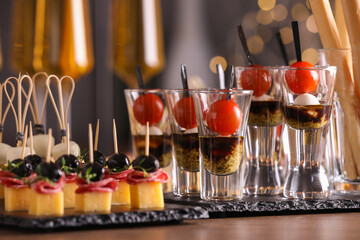 Many different tasty canapes and wine on wooden table against blurred lights