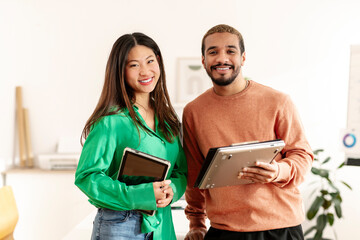 Smiling business colleagues holding wireless technologies and standing in office