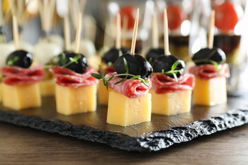 Tasty canapes with cheese, black olives and salami on wooden table, closeup