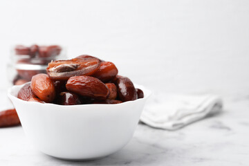 Tasty dried dates in bowl and jar on white marble table, closeup. Space for text