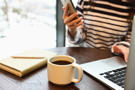 Woman with smartphone having coffee break at wooden table in cafe, closeup - Powered by Adobe