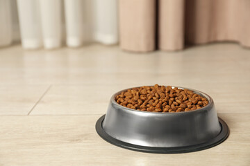 Dry pet food granules in feeding bowl on floor indoors, space for text