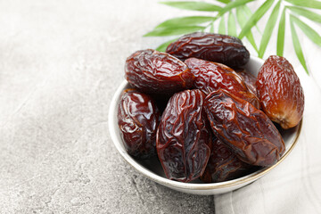 Many tasty dried dates in bowl and leaves on gray textured table, closeup. Space for text