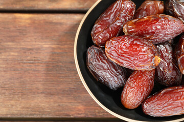 Many tasty dried dates in bowl on wooden table, top view. Space for text