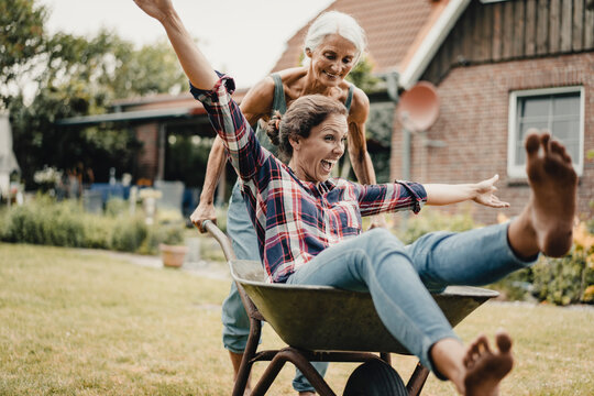 Mother pushing daughter, sitting in push cart, through he garden