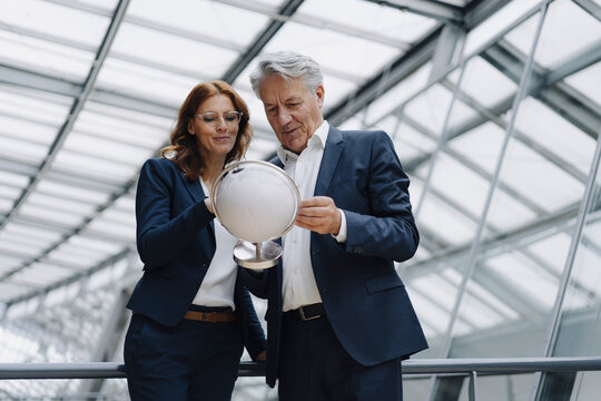 Businessman and businesswoman looking at globe in modern office building