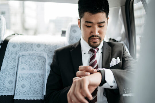Young businessman in a taxi checking the time