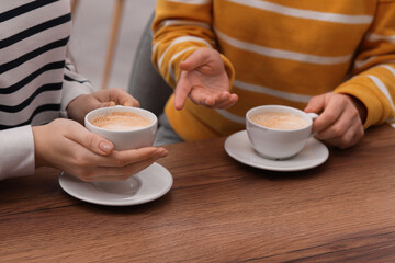 Coffee break. Women with cups of hot drinks at wooden table indoors, closeup