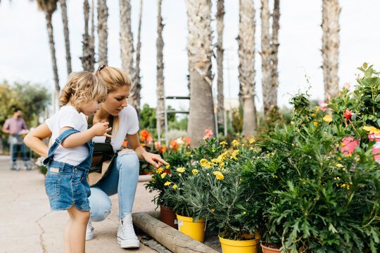 Female worker of a garden center showing flowers to a little girl