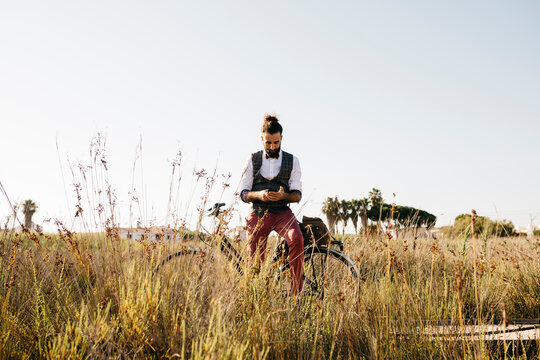 Well dressed man with his bike on a wooden walkway in the countryside using cell phone