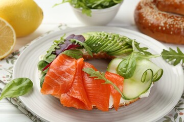 Delicious bagel with salmon, cream cheese, cucumber and avocado on white wooden table, closeup