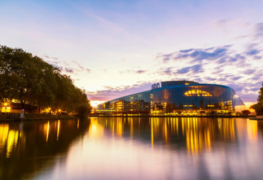 Illuminated Louise Weiss building by river against sky at sunset, Strasbourg, France