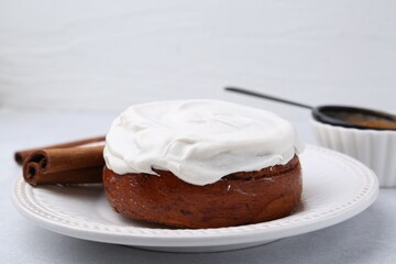 Tasty cinnamon roll with cream and spices on light table, closeup