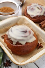 Tasty cinnamon rolls with cream and spices on white wooden table, closeup