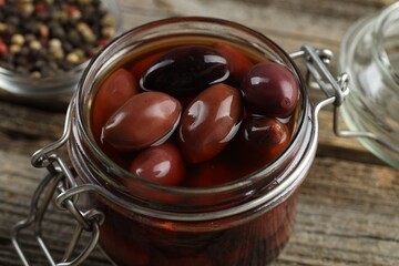 Pickled olives in glass jar and spices on wooden table, closeup