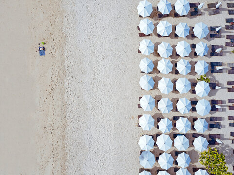 Indonesia, Bali, Aerial view of man sunbathing in front of rows of beach umbrellas on sandy coastal beach of Nusa Dua
