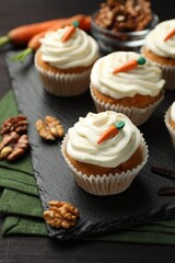Tasty carrot muffins with cream and walnuts on black wooden table, closeup