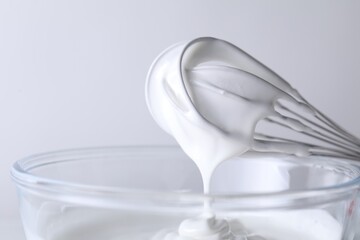 Whisk and bowl with whipped cream on white background, closeup