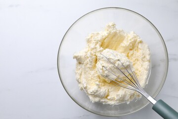 Bowl with whisk and whipped cream on white marble table, top view. Space for text