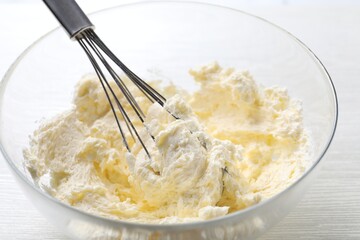 Bowl with whisk and whipped cream on white wooden table, closeup