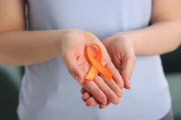 Multiple Sclerosis awareness. Young woman holding orange ribbon indoors, closeup