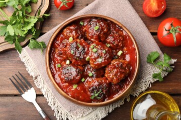 Delicious meatballs with tomato sauce and herbs served on wooden table, flat lay