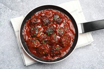 Delicious meatballs with tomato sauce and herbs in on grey table, top view