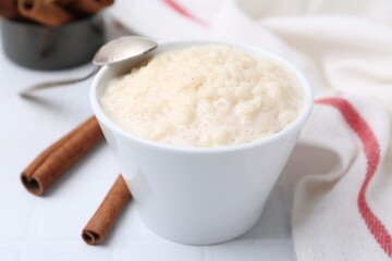 Tasty rice pudding with cinnamon served on white tiled table, closeup