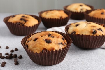 Delicious muffin with chocolate chips on light grey table, closeup