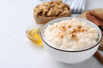 Tasty rice pudding with cinnamon served on white tiled table, closeup