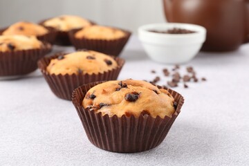 Delicious muffin with chocolate chips on light grey table, closeup