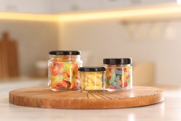 Tasty gummy candies in glass jars on white table