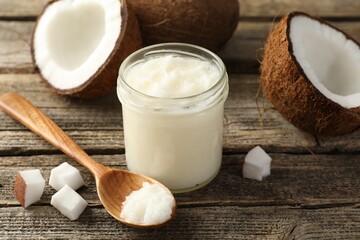Organic coconut cooking oil in glass jar, spoon and fresh fruits on wooden table, closeup