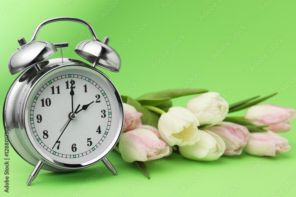 Poster Spring time. Alarm clock and beautiful tulips on green background, closeup