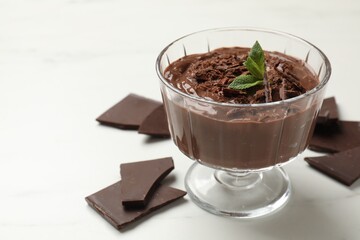 Tasty pudding with mint and pieces of chocolate on white table, closeup